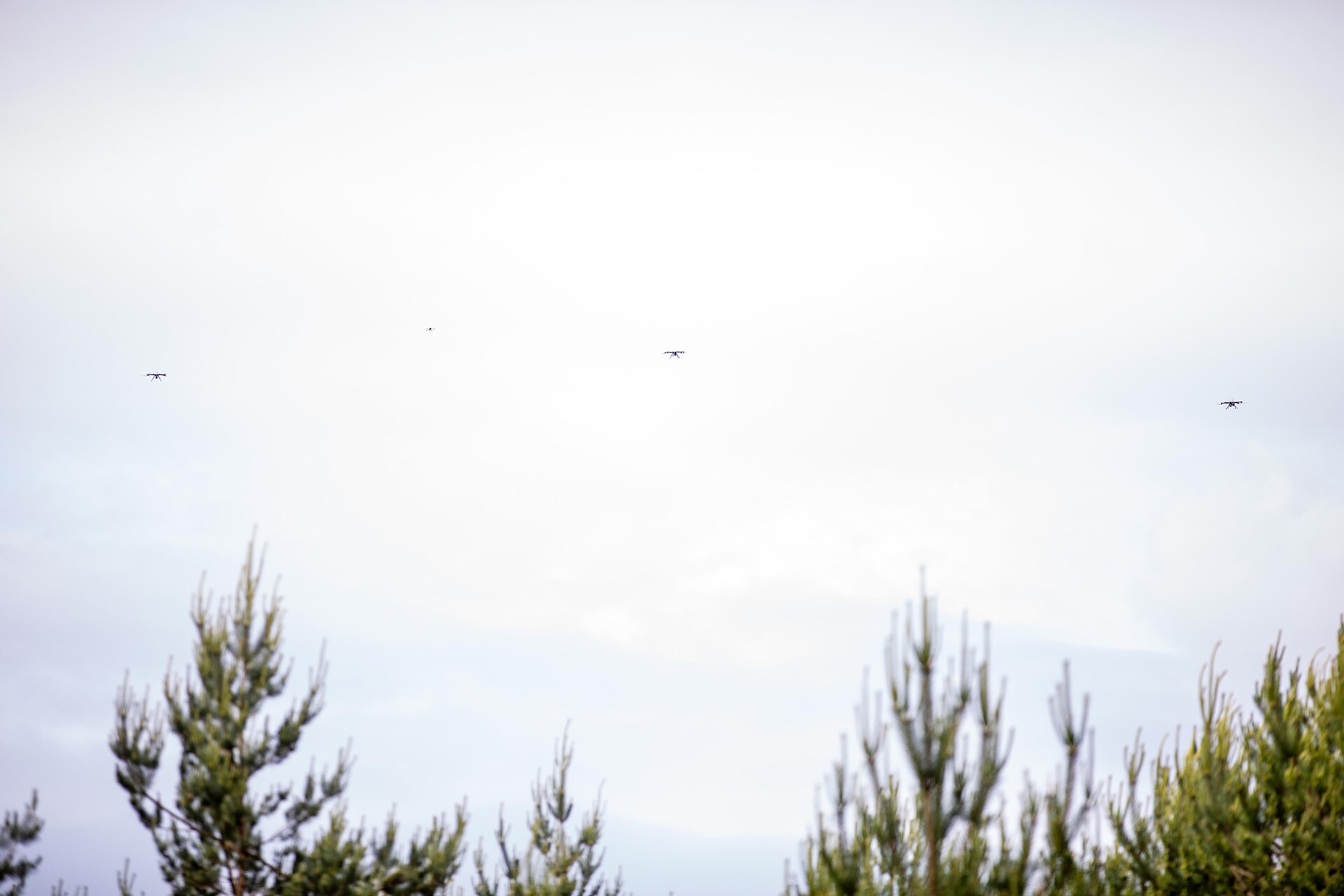 Several small drones flying over a field during a military exercise